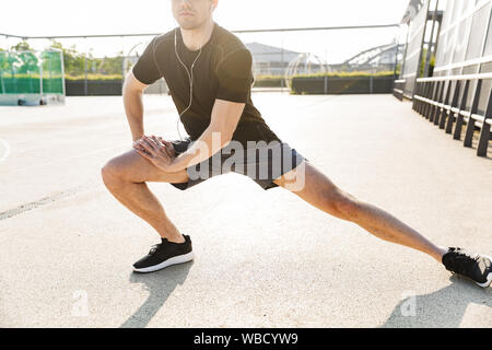 Immagine di uomo bello in sportswear Indossa auricolari formazione sul campo sportivo durante la mattina allenamento all'aperto Foto Stock