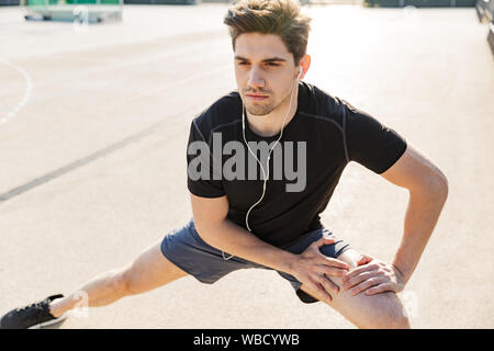 Immagine di bruna uomo in abbigliamento sportivo che indossa gli auricolari formazione sul campo sportivo durante la mattina allenamento all'aperto Foto Stock