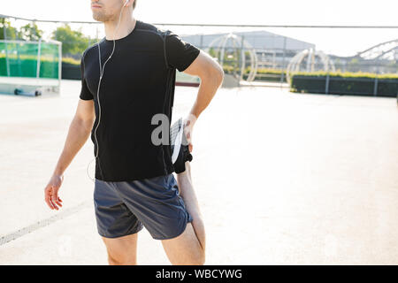 Immagine dell uomo maschile nell'abbigliamento sportivo che indossa gli auricolari formazione sul campo sportivo durante la mattina allenamento all'aperto Foto Stock
