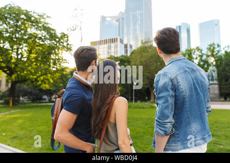 Vista posteriore di un gruppo di giovani amici in piedi presso il parco della città, guardando lontano Foto Stock