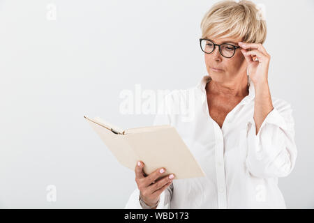 Ritratto di concentrato di donna adulta indossando occhiali lettura prenota isolate su sfondo bianco in studio Foto Stock