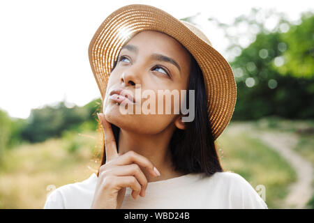 Foto di bella donna che indossa cappello di paglia e il labbro piercing guardando verso l'alto mentre si passeggia in un parco verde Foto Stock