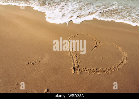 Forma di cuore su una sabbiosa spiaggia balneare disegnato con un bastone di legno Foto Stock