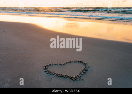 Forma di cuore su una sabbiosa spiaggia balneare disegnato con un bastone di legno al tramonto Foto Stock