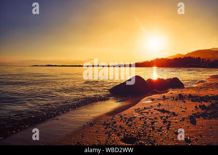 Offre una bellissima vista panoramica sulla spiaggia al tramonto, illuminato dalla luce del sole serale contro lo sfondo delle bellissime montagne grandi, lussuose summ Foto Stock