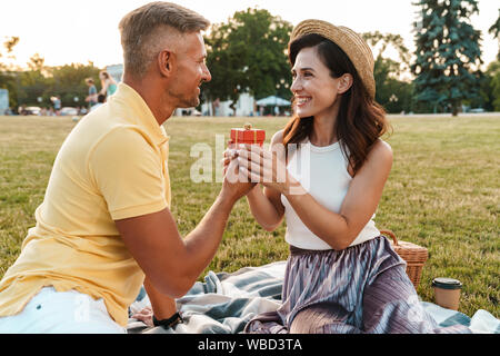 Immagine di felice uomo di mezza età dando presente casella a bella donna seduti su erba in estate park Foto Stock