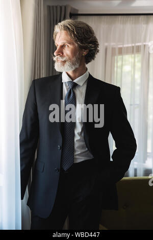 Immagine di un grave concentrata barbuto coppia bello grey-haired imprenditore che pongono al chiuso in casa vicino alla finestra vestito in abiti formali. Foto Stock