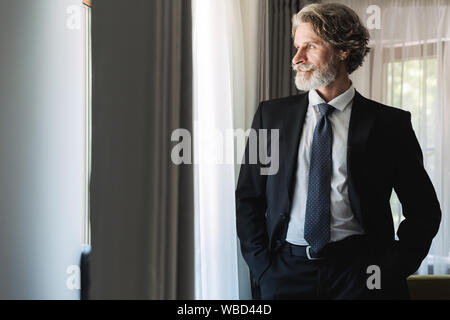 Immagine di un grave concentrata barbuto coppia bello grey-haired imprenditore che pongono al chiuso in casa vicino alla finestra vestito in abiti formali. Foto Stock