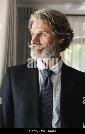 Immagine di un grave concentrata barbuto coppia bello grey-haired imprenditore che pongono al chiuso in casa vicino alla finestra vestito in abiti formali. Foto Stock