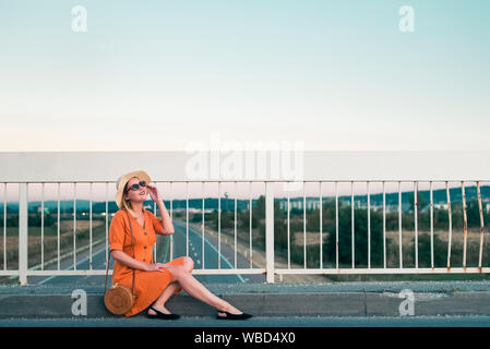 Giovane donna seduta in abito arancione sul ponte Foto Stock