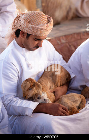 Un uomo in abbigliamento tradizionale azienda due capre marrone nel suo giro al mercato del bestiame, Nizwa, Sultanato di Oman Foto Stock