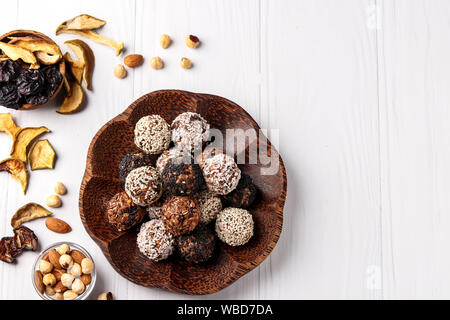 Le sfere di energia di dadi, fiocchi d'avena e frutta secca con lino e i semi di sesamo, fiocchi di cocco su un piatto in legno di noce di cocco su sfondo bianco Foto Stock