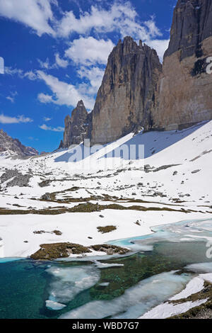 I picchi delle Tre Cime di Lavaredo nelle Dolomiti, Italia, cielo blu con nuvole alcuni, un sacco di neve sul terreno e parzialmente laghetto congelato in giugno. Foto Stock