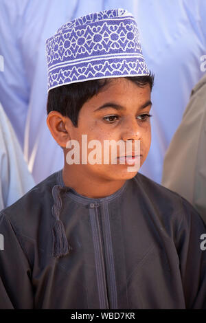 Ritratto di giovane ragazzo in abiti tradizionali che indossa il cappuccio ricamato al mercato del bestiame, Nizwa, Sultanato di Oman Foto Stock