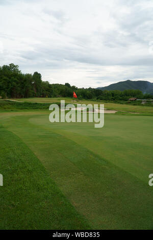 Bandiera rossa e verde erba bunker di sabbia al bellissimo campo da golf a lato della montagna Foto Stock