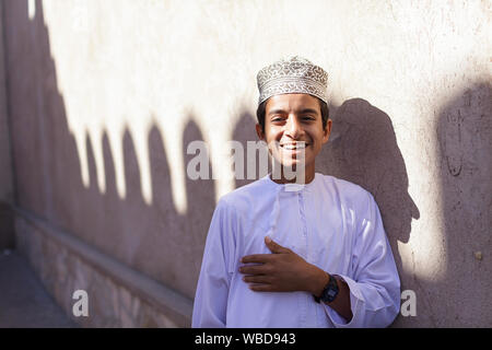 Ritratto di giovane ragazzo in abiti tradizionali che indossa il cappuccio ricamato sorridente sulla strada di Nizwa, Sultanato di Oman Foto Stock