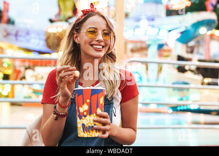 Immagine positiva di un giovane donna bionda nel parco dei divertimenti di mangiare popcorn. Foto Stock