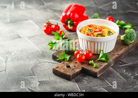 Frittata con broccoli forma ceramica. Frittata con i broccoli, dolci peperoni e pomodori in due forme ceramiche per la cottura. Omelette italiano con vege Foto Stock