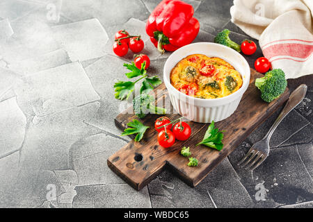 Frittata con broccoli in forma di ceramica. Frittata con i broccoli, dolci peperoni e pomodori in due forme ceramiche per la cottura. Omelette italiano con v Foto Stock