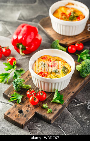 Frittata con broccoli in due forme ceramiche. Frittata con i broccoli, dolci peperoni e pomodori in due forme ceramiche per la cottura. Omelette italiano w Foto Stock