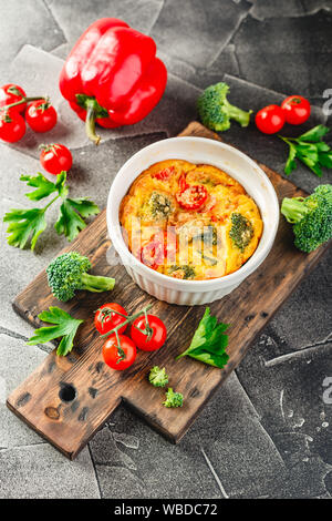 Frittata con broccoli in forma di ceramica. Frittata con i broccoli, dolci peperoni e pomodori in due forme ceramiche per la cottura. Omelette italiano con v Foto Stock