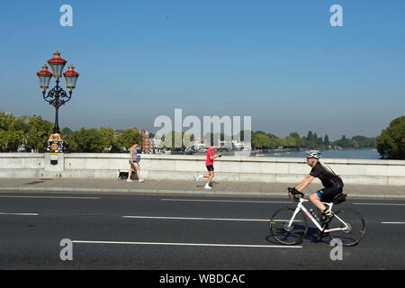 Ciclista maschio attraversare Putney Bridge, Londra, Inghilterra, con un pareggiatore di maschio e femmina pedone in background Foto Stock