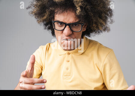 Foto di furiosa uomo caucasico con acconciatura afro accigliata e mostrando il dito pistola gesto isolato su sfondo grigio Foto Stock