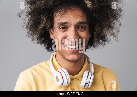 Foto di gioiosa uomo caucasico con acconciatura afro indossa le cuffie sorridente in telecamera isolate su uno sfondo grigio Foto Stock