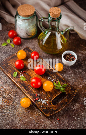 Il giallo e il rosso del pomodoro ciliegino, una bottiglia di olio di oliva, sale, pepe e basilico Foto Stock