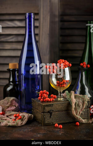 Autunno ancora in vita con rowan bacche, un bicchiere di vetro, bottiglie di vino e una scatola di legno su uno sfondo scuro Foto Stock