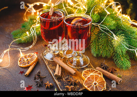 Le coppe di vetro di vin brulé con spezie e arancio secco di pezzi sul tagliere di legno su sfondo scuro. Tradizionale bevanda di Natale Foto Stock