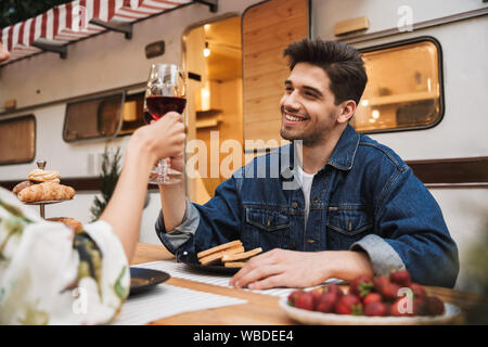 Ritratto di coppia felice l uomo e la donna di bere il vino rosso mentre mangiando panini insieme al tavolo di legno all'aperto Foto Stock