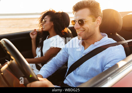 Bella sorridente giovane coppia multietnica di equitazione in una cabriolet Foto Stock