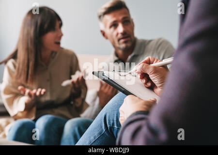 Foto di perplesso irritato giovane uomo e donna una conversazione con lo psicologo sulla sessione di terapia in camera Foto Stock