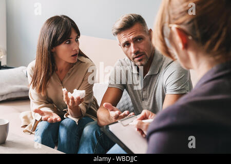 Foto di perplesso infelice giovane uomo e donna una conversazione con lo psicologo sulla sessione di terapia in camera Foto Stock