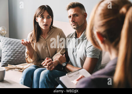 Foto di perplesso caucasian giovane uomo e donna una conversazione con lo psicologo sulla sessione di terapia in camera Foto Stock