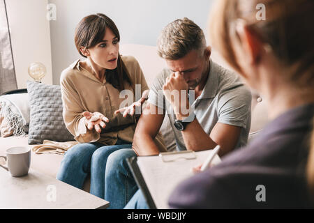 Foto di perplesso infastiditi giovane uomo e donna una conversazione con lo psicologo sulla sessione di terapia in camera Foto Stock
