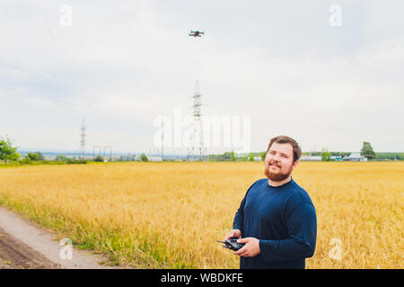 Agricoltore detiene remote controller con le sue mani mentre quadcopter è volare su sfondo. Drone vola dietro l'agronomo nel campo di grano. Agricultura Foto Stock