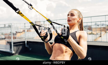 Giovane donna esercita su un tetto. Atleta femminile utilizzando le cinghie di sospensione. Foto Stock