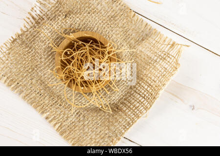 Lotto di pezzi di sottile pasta tagliatelle in ciotola di legno su stoffa di iuta flatlay su legno bianco Foto Stock