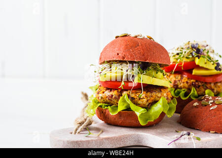 Rosa hamburger vegano con fagioli cotoletta, avocado e piantine su uno sfondo bianco. Foto Stock