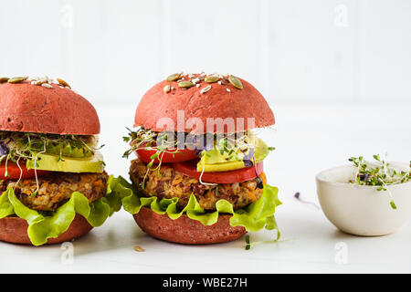 Rosa hamburger vegano con fagioli cotoletta, avocado e piantine su uno sfondo bianco. Foto Stock