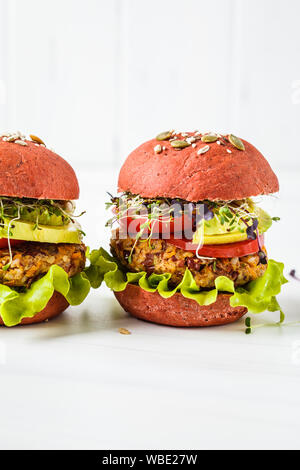 Rosa hamburger vegano con fagioli cotoletta, avocado e piantine su uno sfondo bianco. Foto Stock