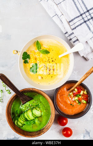 Tre differenti crema di verdure minestre in bocce su sfondo grigio. Il mais, il cetriolo e gazpacho zuppe. Foto Stock