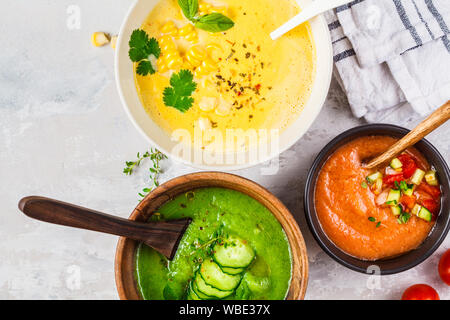 Tre differenti crema di verdure minestre in bocce su sfondo grigio. Il mais, il cetriolo e gazpacho zuppe. Foto Stock
