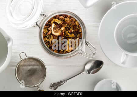 Cumulo di frutta secca di infusione del tè con arance e fragole miscelato con foglie di tè e un assortimento di erbe in vetro bianco sul tavolo di legno con sfondo Foto Stock