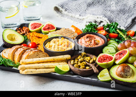 Vegano antipasto. Hummus, tofu, verdure, frutta e pane su un vassoio nero, sfondo bianco. Foto Stock