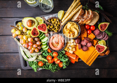 La carne e i formaggi antipasto. Salsicce, formaggio, hummus, verdure, frutta e pane su un vassoio nero, sfondo scuro. Foto Stock