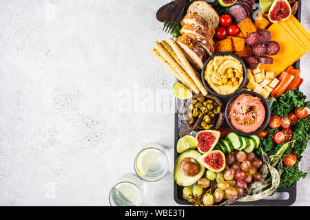 La carne e i formaggi antipasto. Salsicce, formaggio, hummus, verdure, frutta e pane su un vassoio nero, sfondo bianco, copia dello spazio. Foto Stock