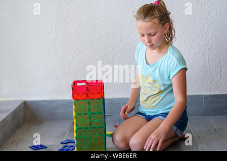 Bella ragazza adolescente giocando con un sacco di colorati di materia plastica in blocchi costruttore e costruisce la casa. Foto Stock